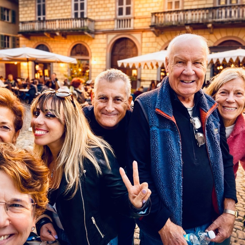 Group selfie of happy people outdoors, with cafes in the background.