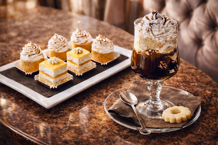 Plated desserts and a whipped cream-topped glass on a table with a cookie and spoon.
