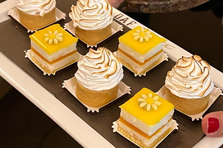 Person holding tray of mini desserts with meringue and yellow flower toppings.