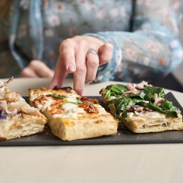 Woman in floral blouse reaching for assorted rectangular pizzas on a plate.