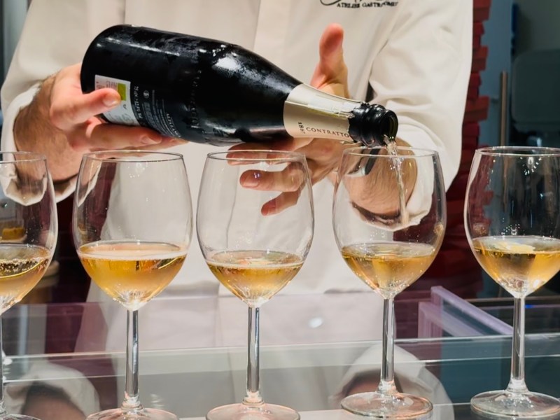 Person in white pouring champagne into wine glasses on a bar countertop.