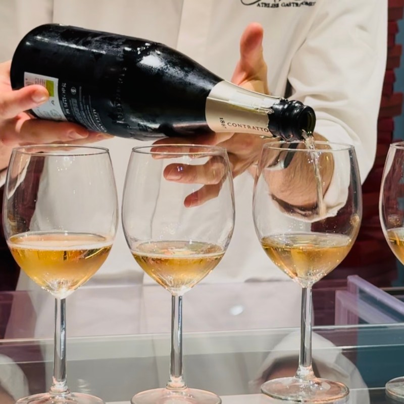 Person in white pouring champagne into wine glasses on a bar countertop.