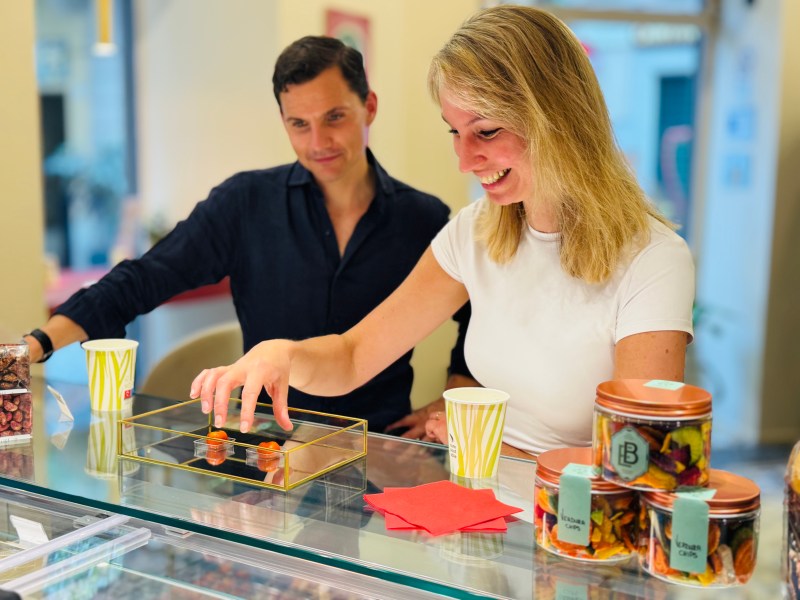 Smiling woman selecting pastries from a display case while a man watches in a shop.