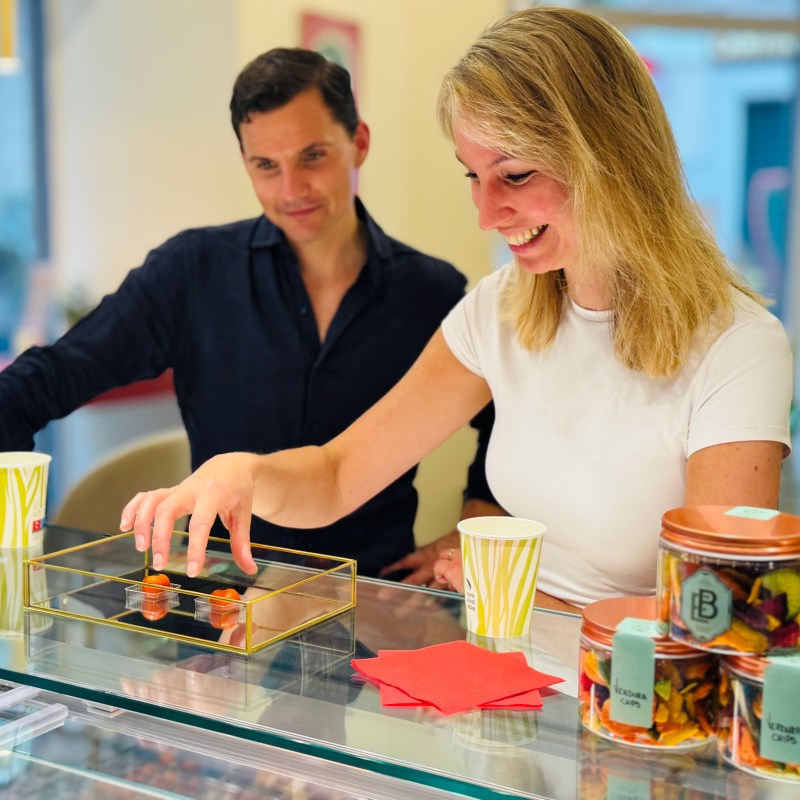Smiling woman selecting pastries from a display case while a man watches in a shop.
