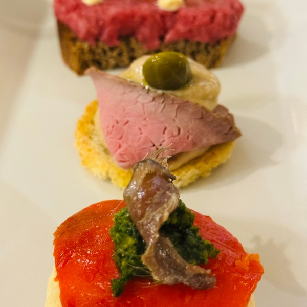 Three appetizers on a plate with toppings of beef, fish, and mousse.