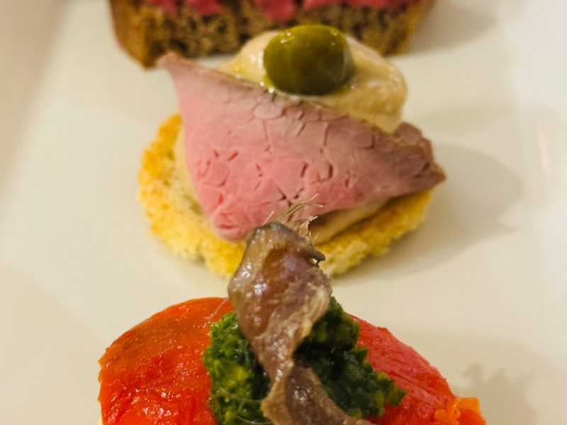 Three appetizers on a plate with toppings of beef, fish, and mousse.