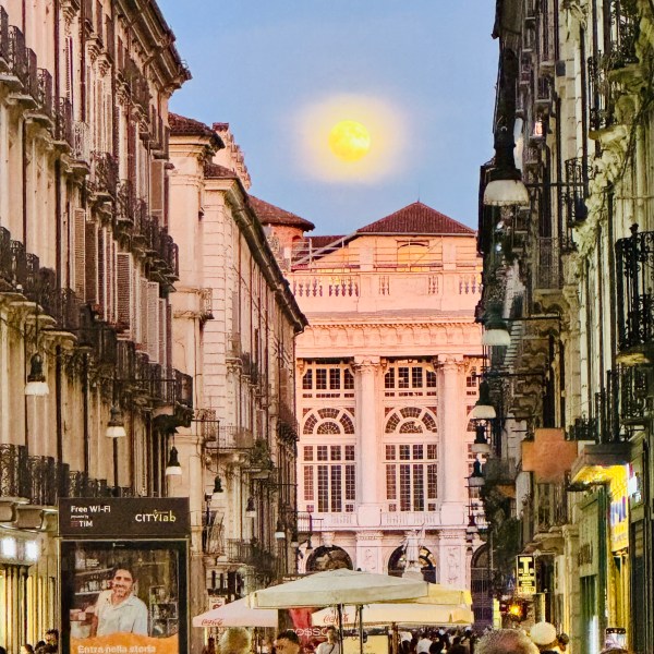 Street view with a full moon above a white historic building at dusk.