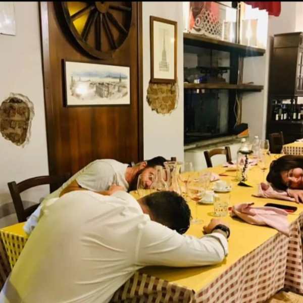 Three people asleep at a dining table in a restaurant with drinks and tableware.