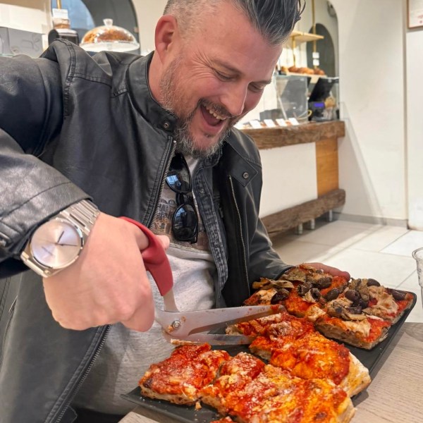 Person cutting rectangular pizzas with scissors, smiling in a cafe.