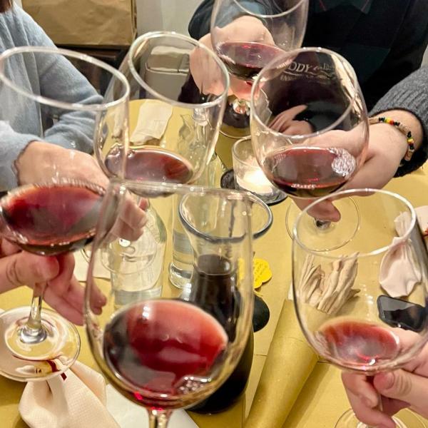 Six people toasting with red wine glasses at a table with yellow tablecloth.