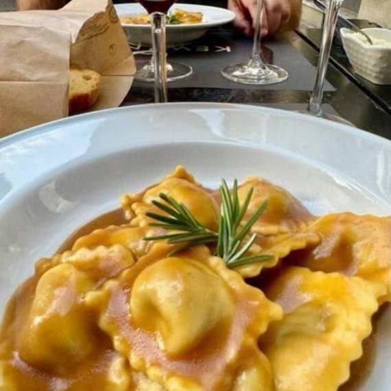 Ravioli with sauce and rosemary garnish on a plate with wine glasses in the background.