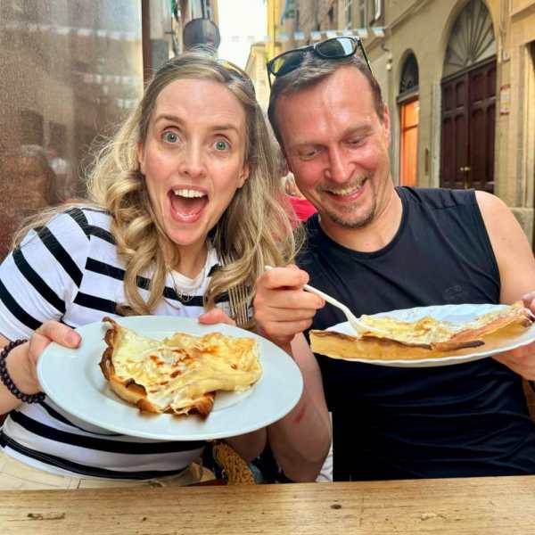 Two happy people holding plates of crepes at an outdoor café.