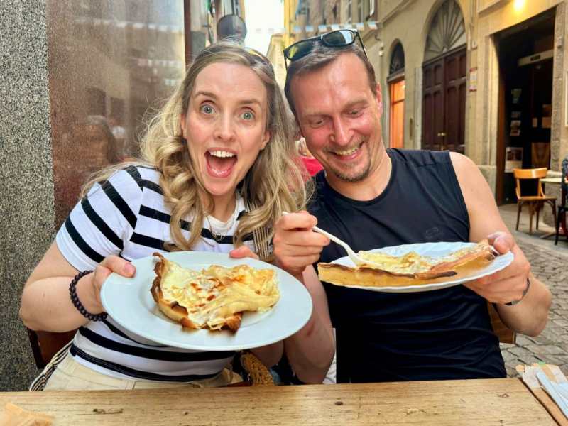 Two happy people holding plates of crepes at an outdoor café.