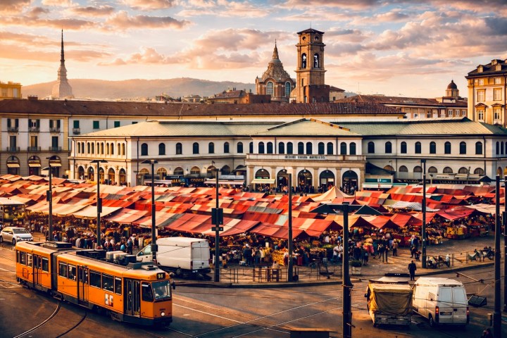 Bustling outdoor market with red canopies, historic buildings, and orange tram at sunset.