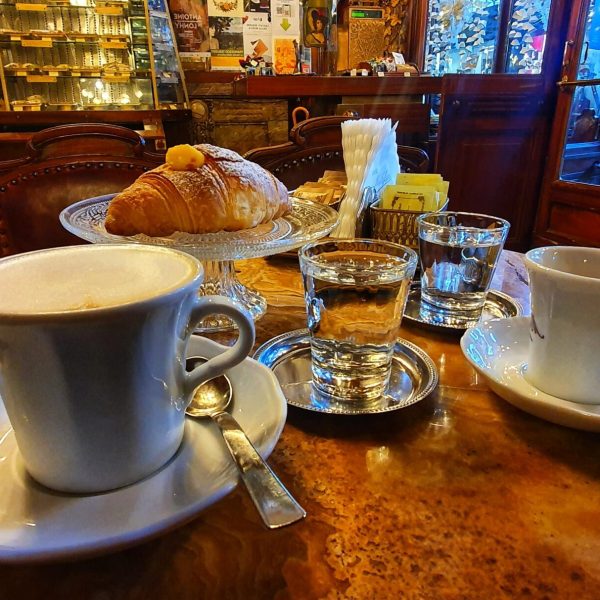 Cozy cafe table with cappuccinos, croissant, and glassware.