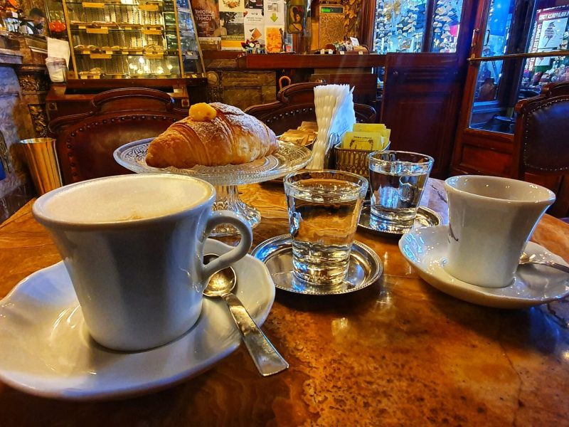 Cozy cafe table with cappuccinos, croissant, and glassware.