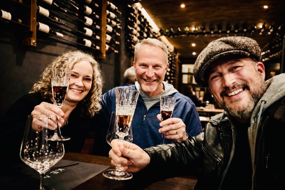 Three people smiling and toasting with wine glasses in a wine cellar.