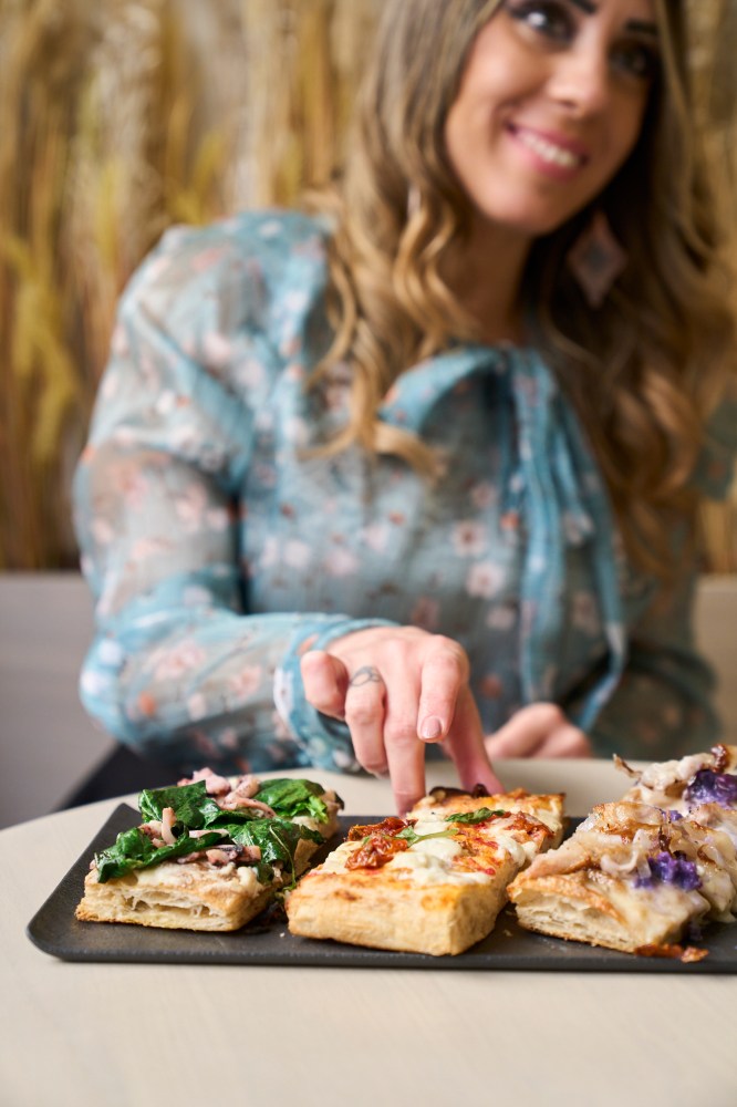 a woman sitting at a table with a plate of pizza and focaccia