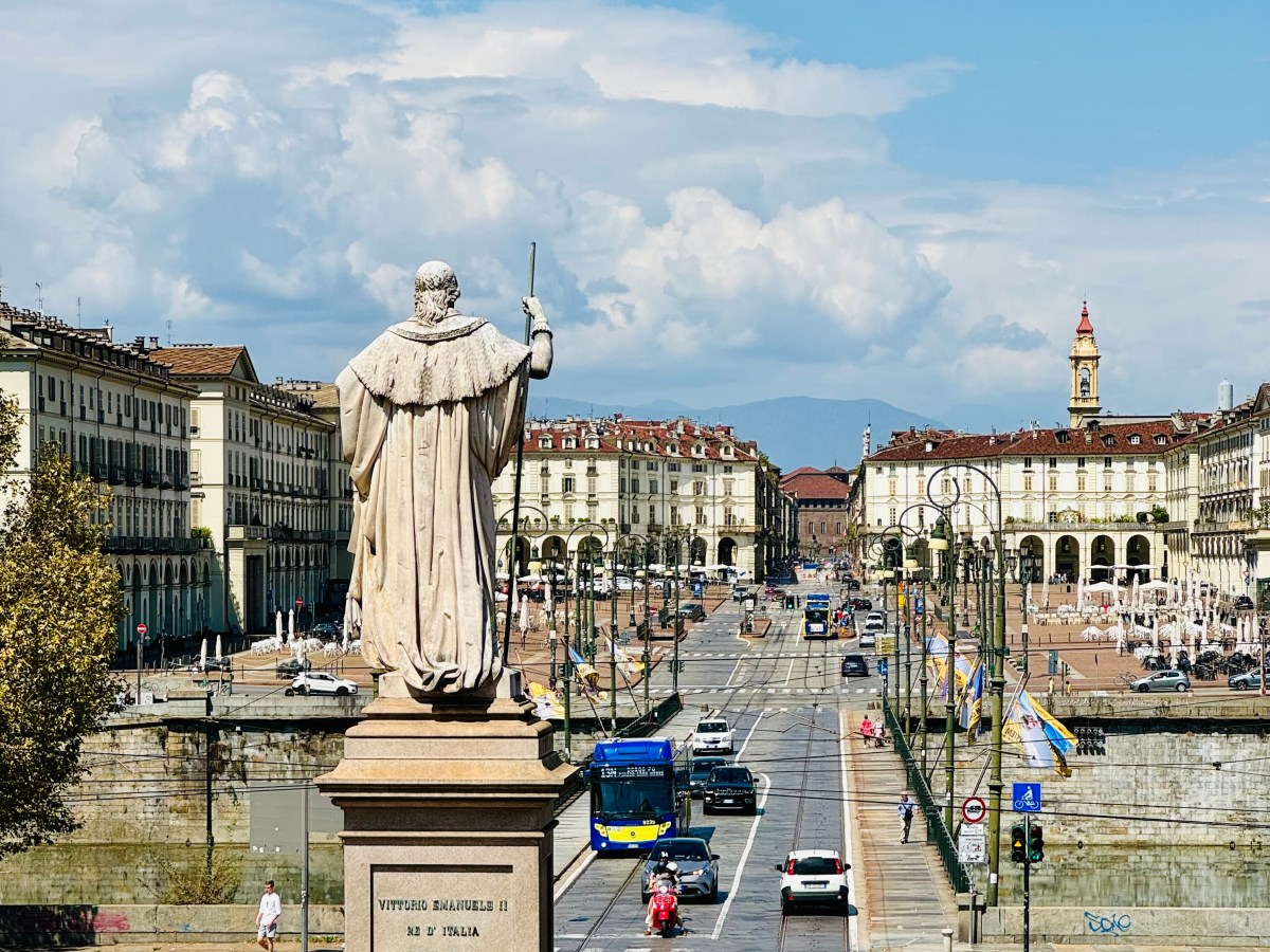 Statue overlooking busy street with vehicles and historic buildings under a blue sky.