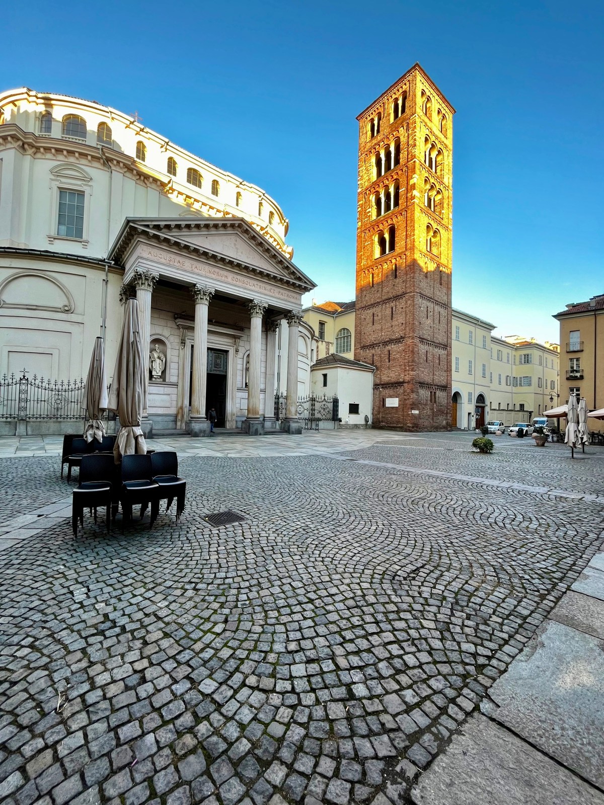 Historic brick tower and church in cobblestone plaza under clear blue sky.