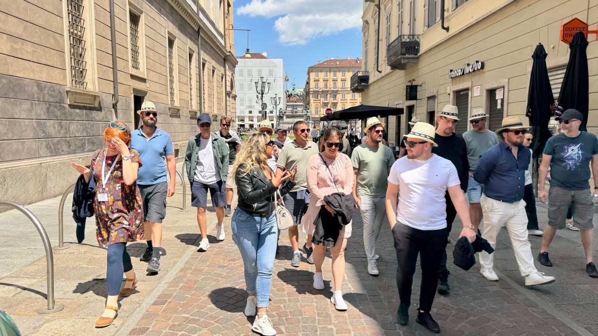 Group of people walking on a sunny city street, wearing casual summer clothes and hats.