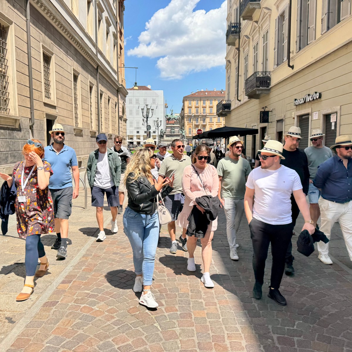 Group of people walking on a sunny city street, wearing casual summer clothes and hats.