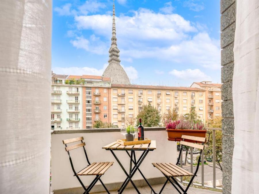 Balcony view with table, chairs, wine, snacks, and urban skyline featuring distinctive tower.