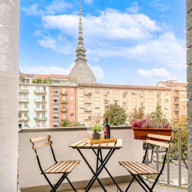 Balcony view with table, chairs, wine, snacks, and urban skyline featuring distinctive tower.