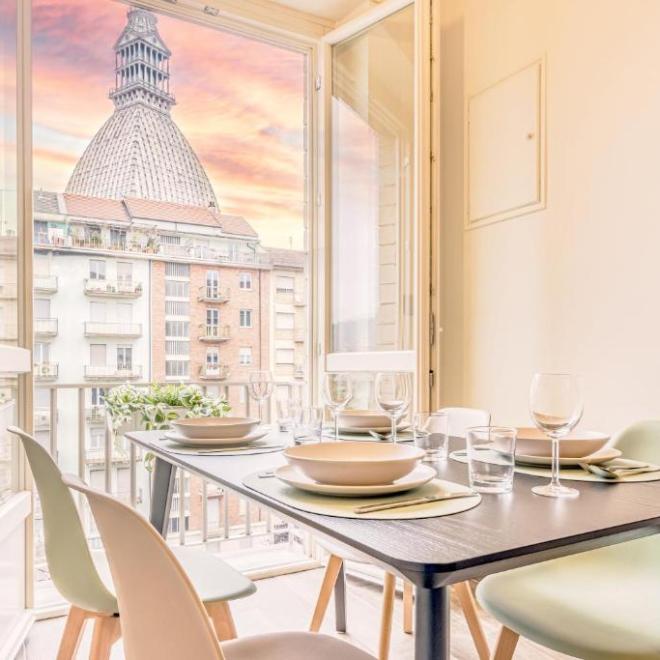 Dining table set with plates, glasses in front of an open window with city view and dome.