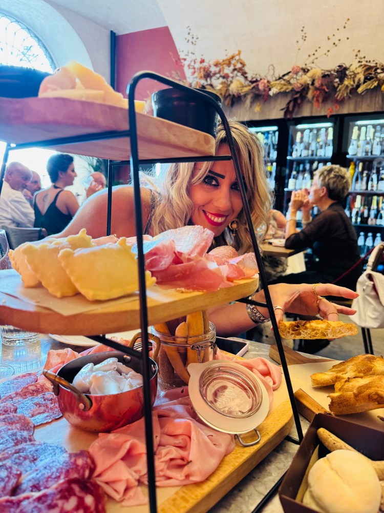 Woman smiling at table with cheese, meats, and bread in restaurant setting.
