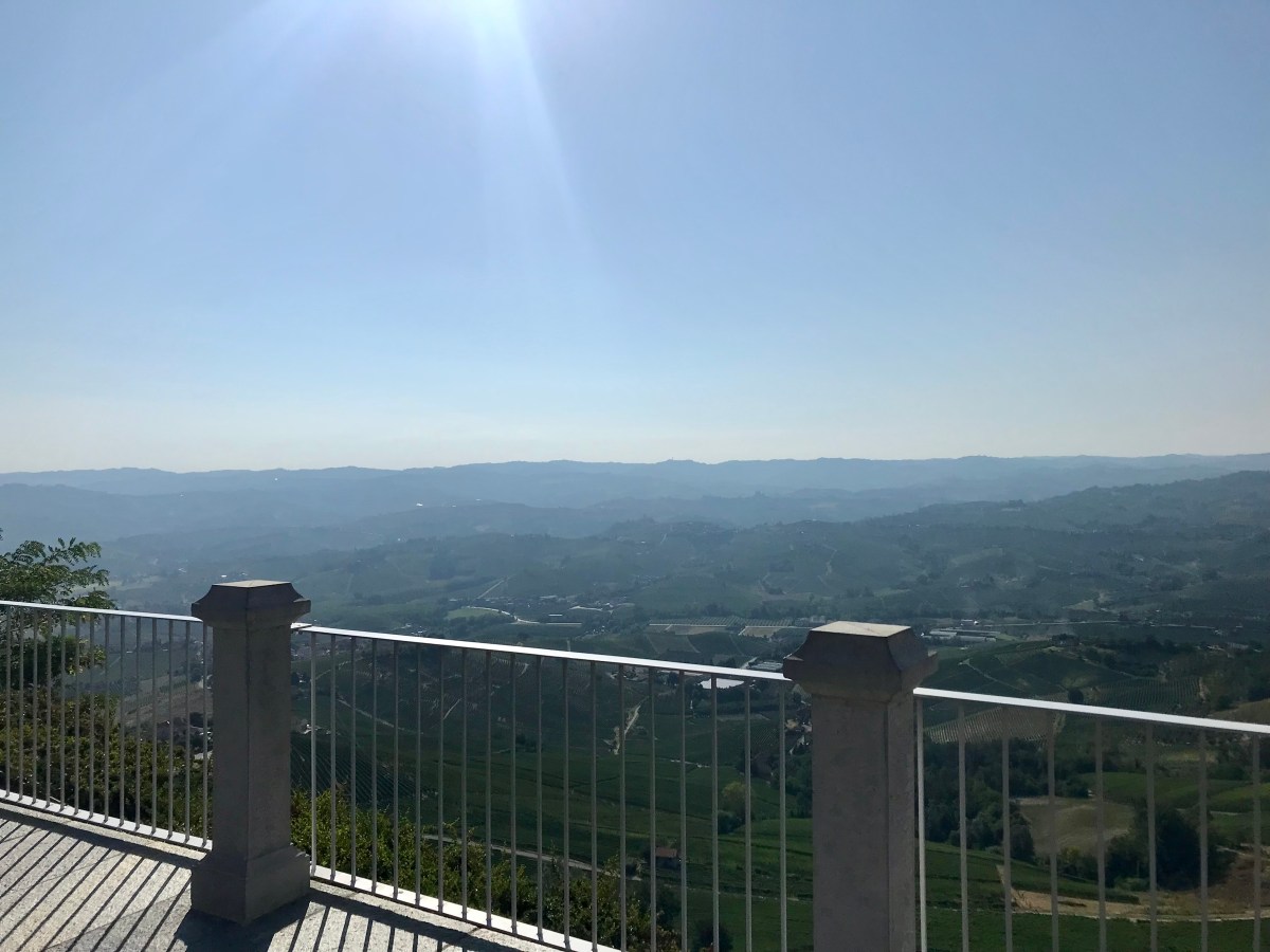 View from a white railing porch over expansive green hills under a sunny blue sky.