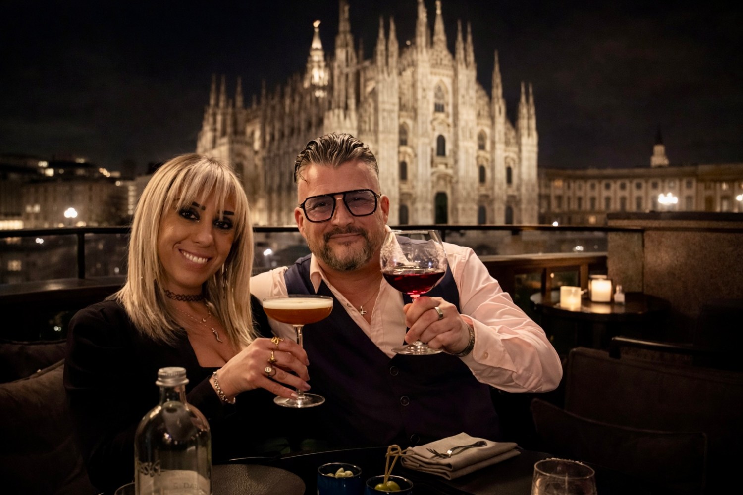 Two people toasting with drinks in front of a gothic cathedral at night.
