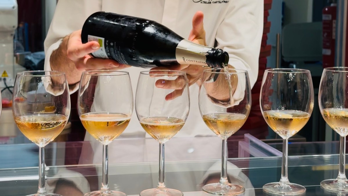 Person pouring sparkling wine into six glasses on a counter.