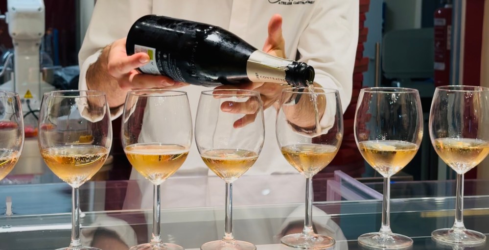 Person pouring sparkling wine into six glasses on a counter.