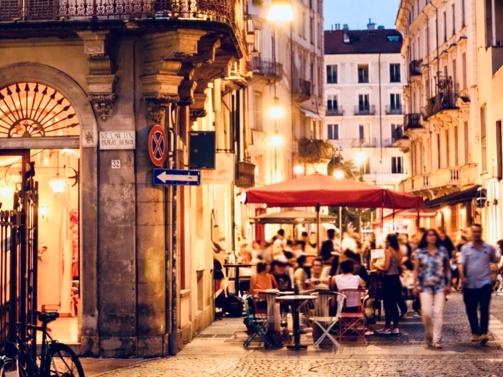 Bustling European street at dusk with outdoor dining and historic architecture.