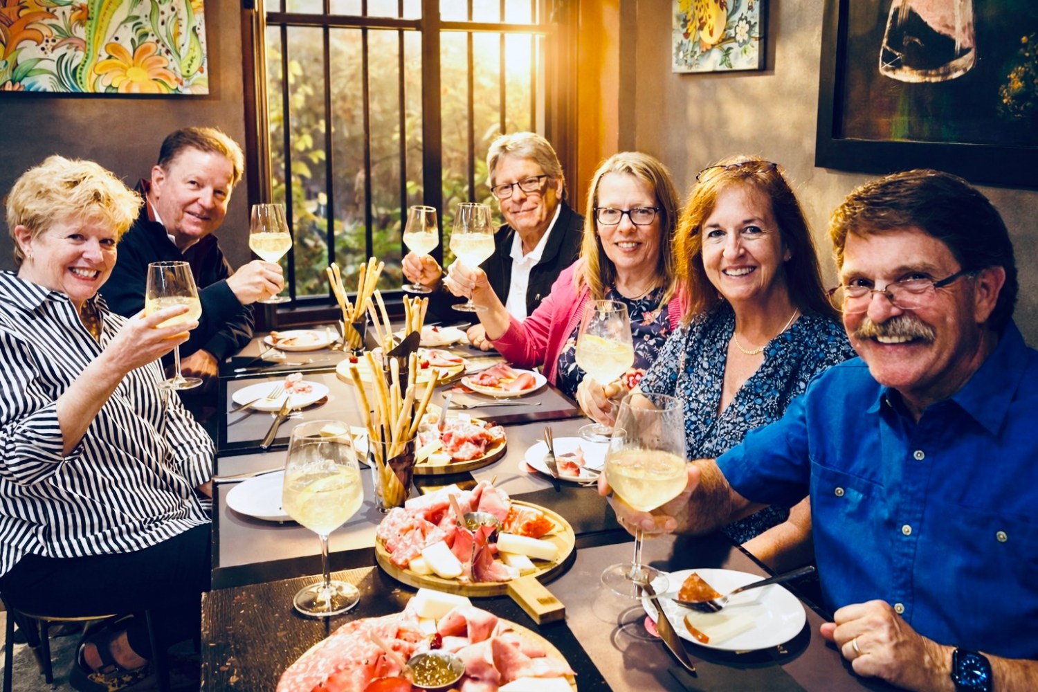 Six people toasting with wine glasses around a table filled with food.