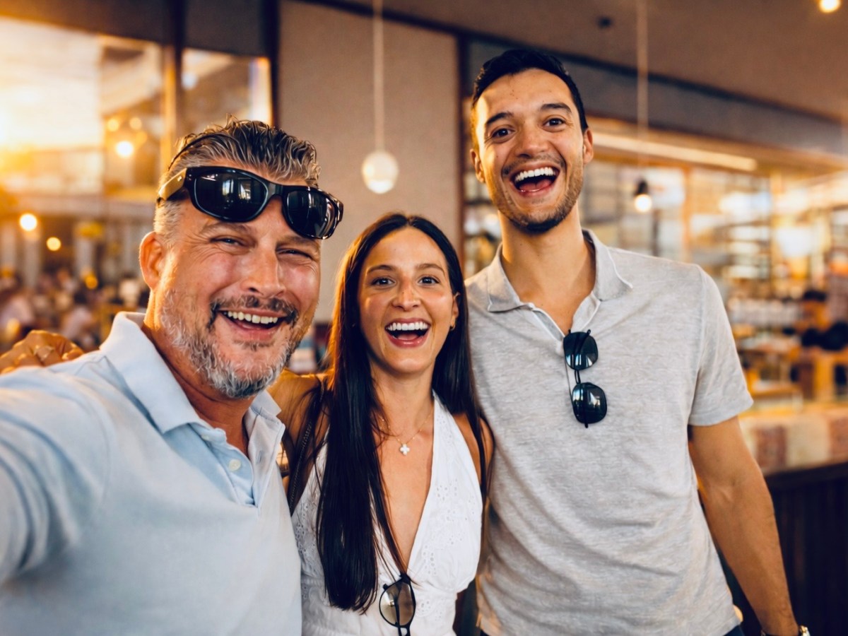 Three people smiling and posing for a selfie in an indoor setting with warm lighting.