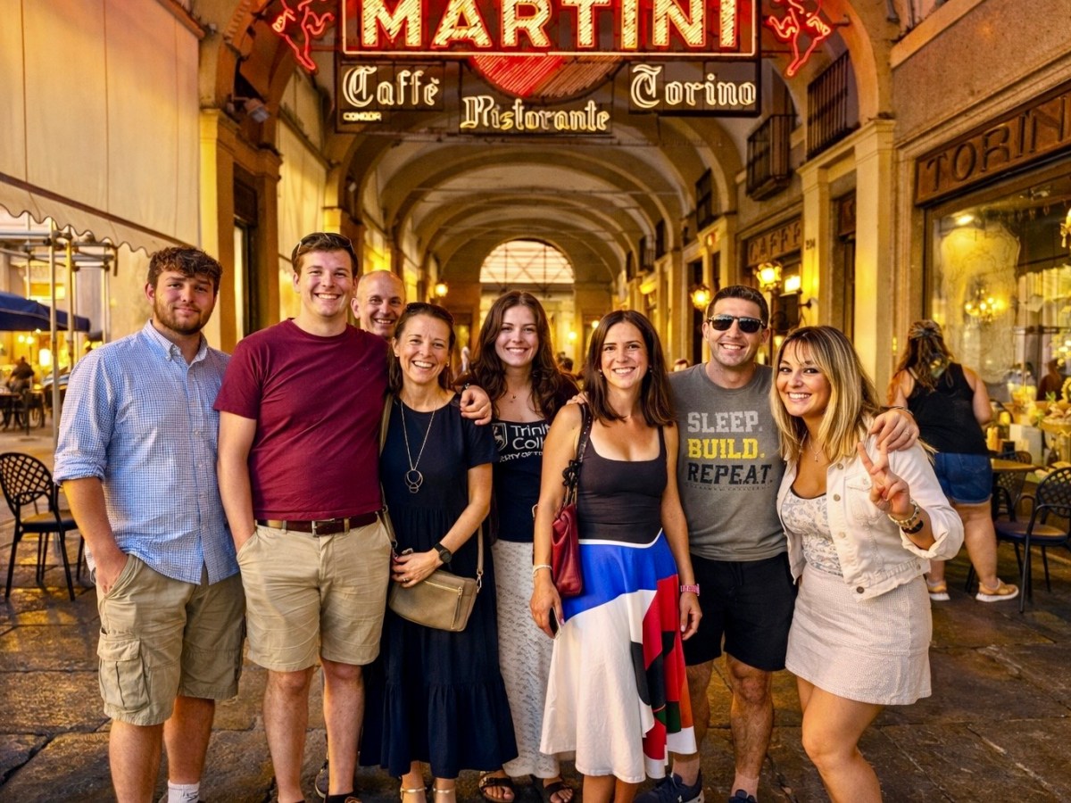 Group of people smiling under a 'Martini' cafe sign in a brightly lit arched passageway.