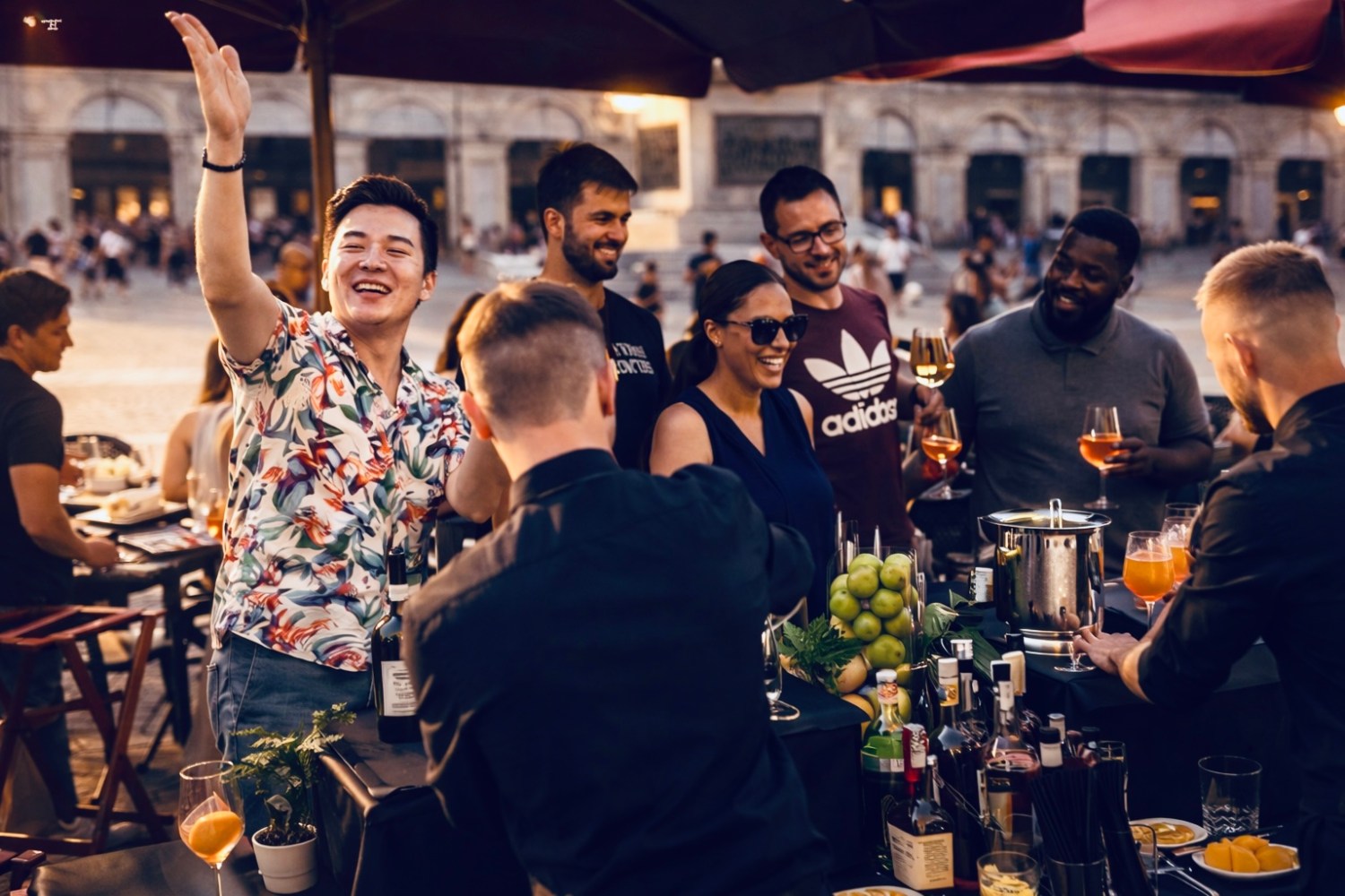 Group of people smiling and talking at an outdoor bar with drinks and fruits on the counter.