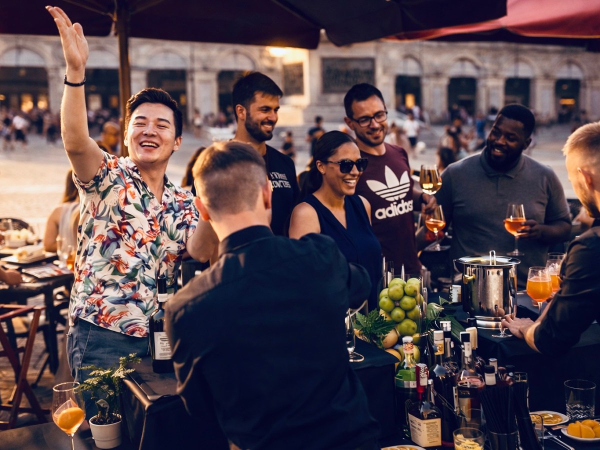 Group of people smiling and talking at an outdoor bar with drinks and fruits on the counter.