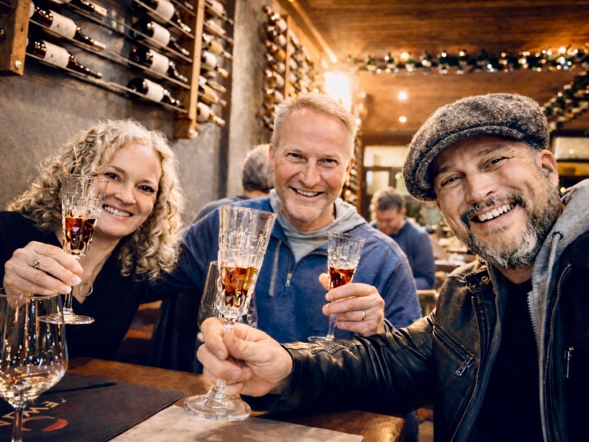Three people smiling and toasting with wine glasses in a cozy setting.