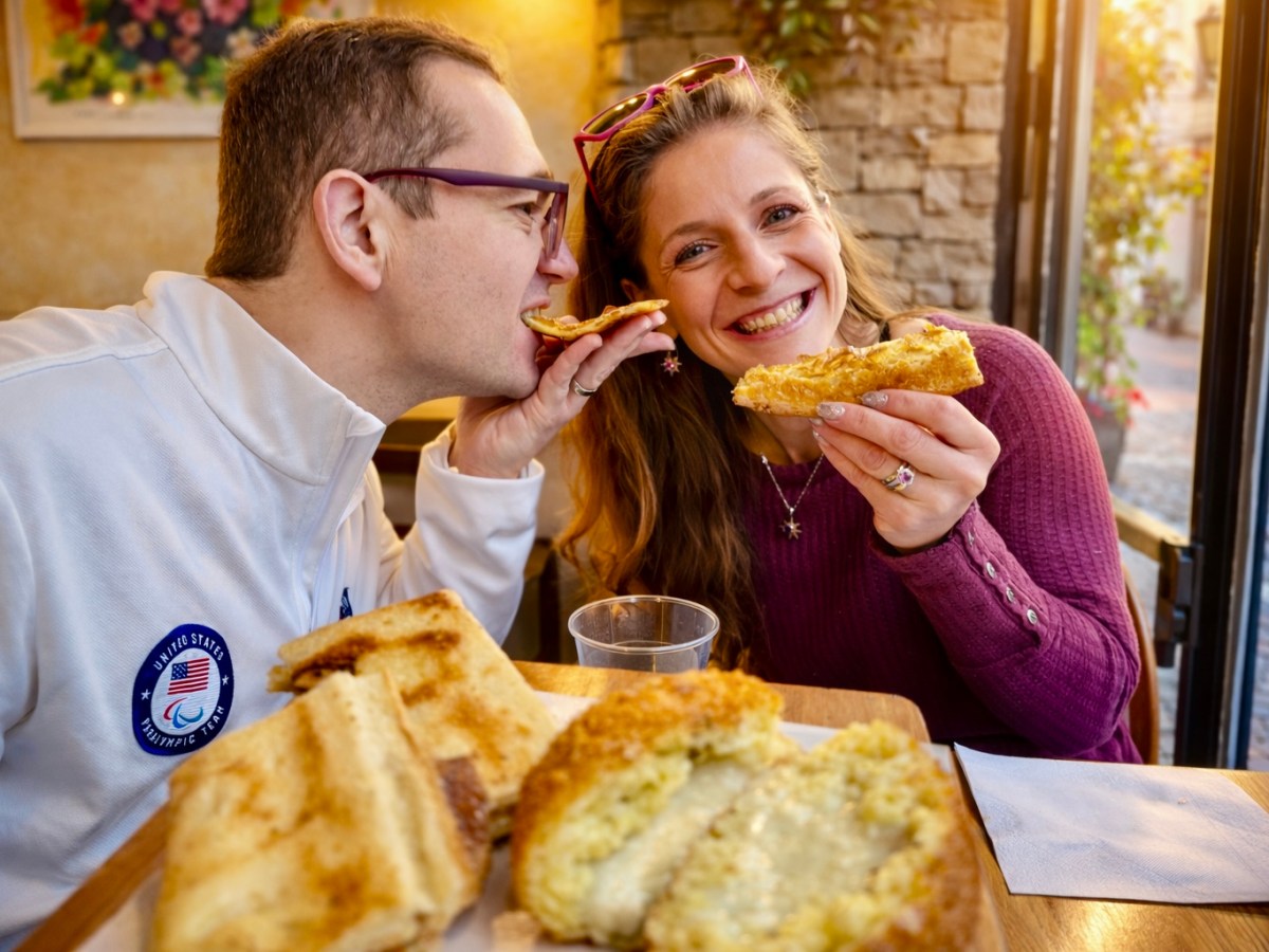 Smiling couple sharing toasted sandwiches at a cafe table.