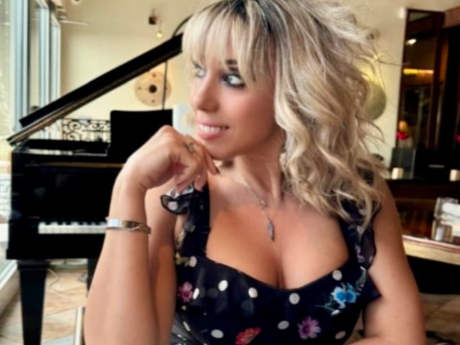 Woman with blonde hair in a black dress sits by a piano in a restaurant.