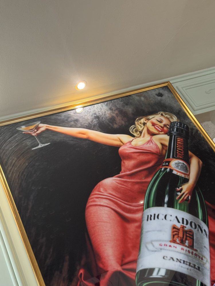 Framed artwork of woman in red dress holding a drink, with a large bottle in the foreground.