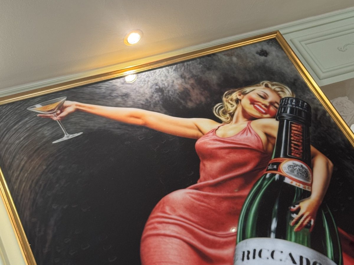Framed artwork of woman in red dress holding a drink, with a large bottle in the foreground.