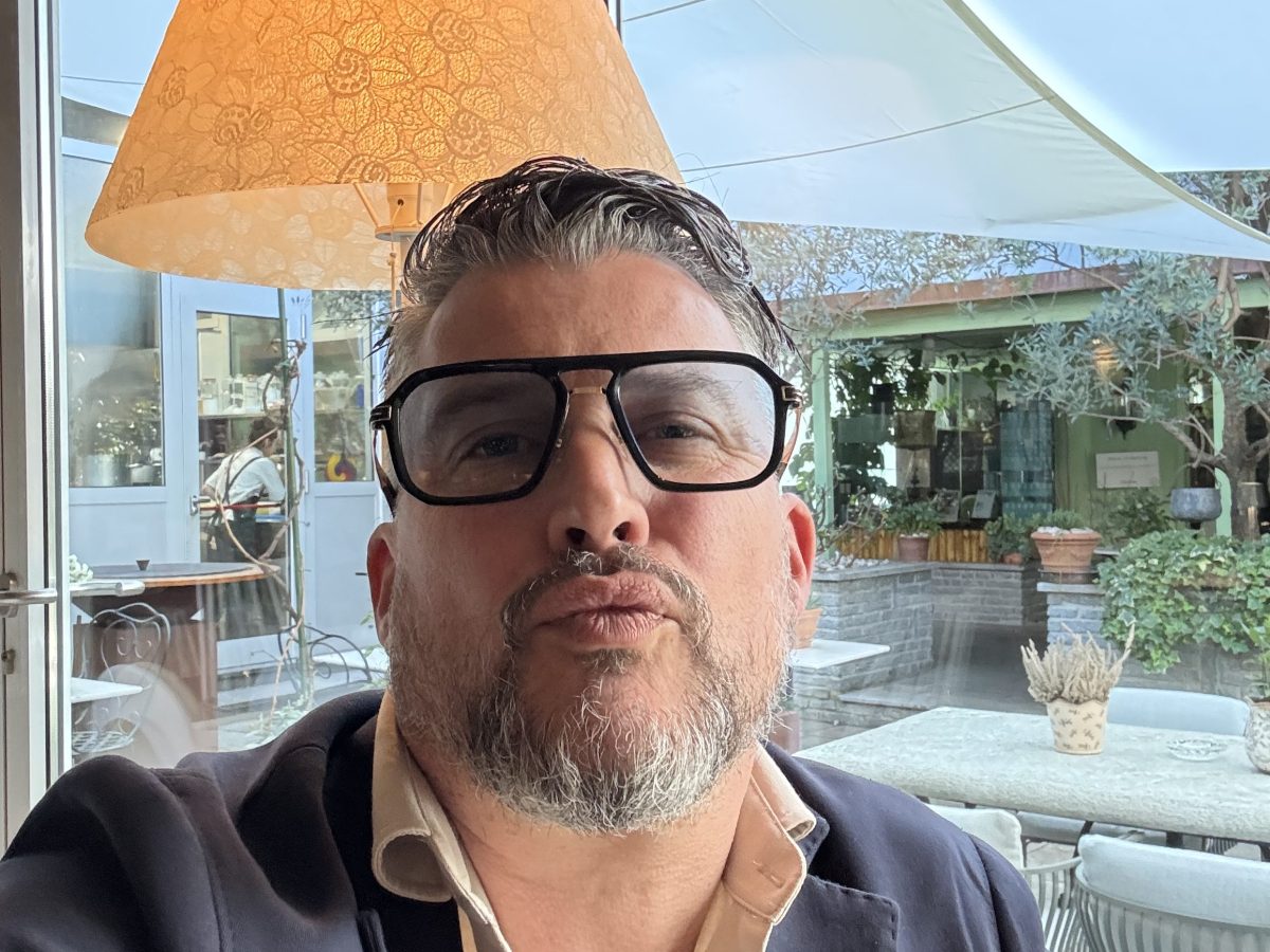 Man with glasses and beard making a duck face indoors with a lamp behind him.