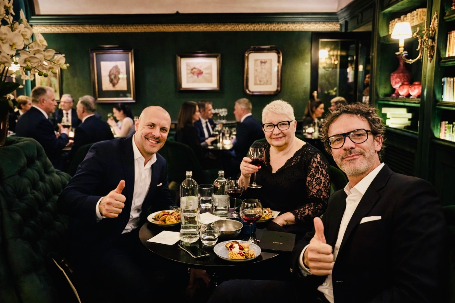 Three people in a restaurant, smiling and giving thumbs up at a table with drinks.