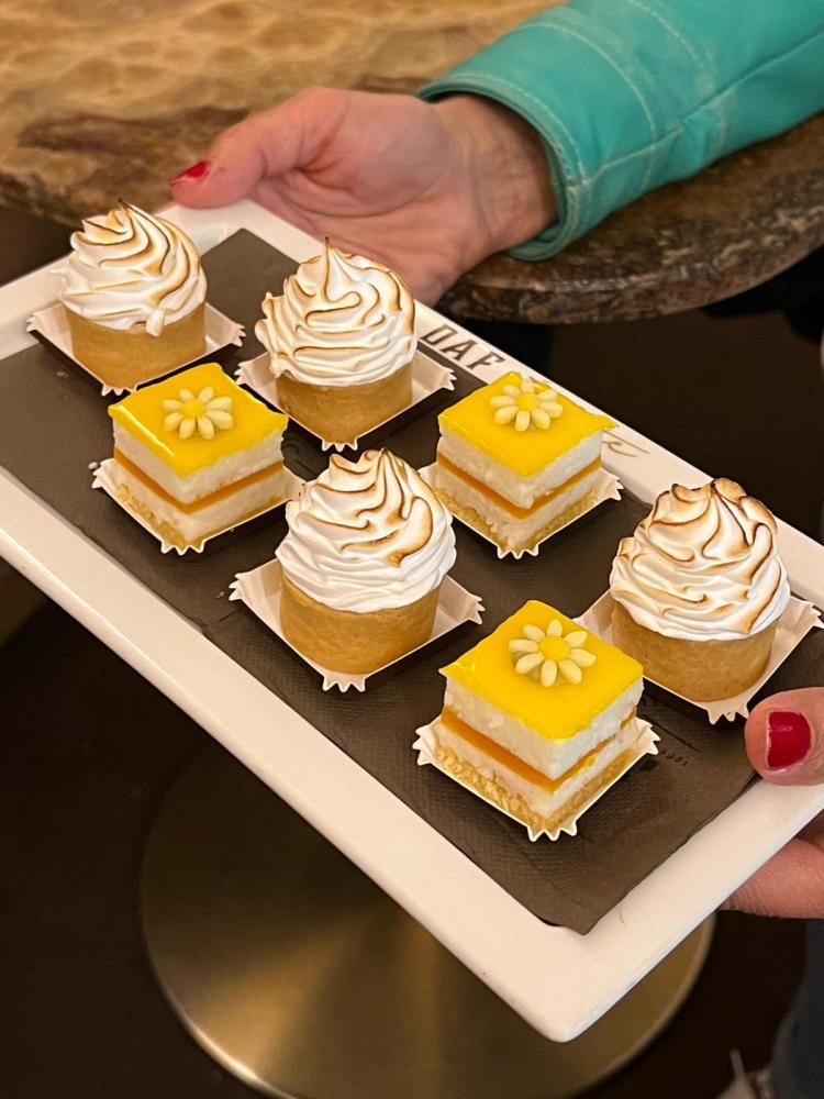 Tray with assorted lemon desserts held by hands with red nails.