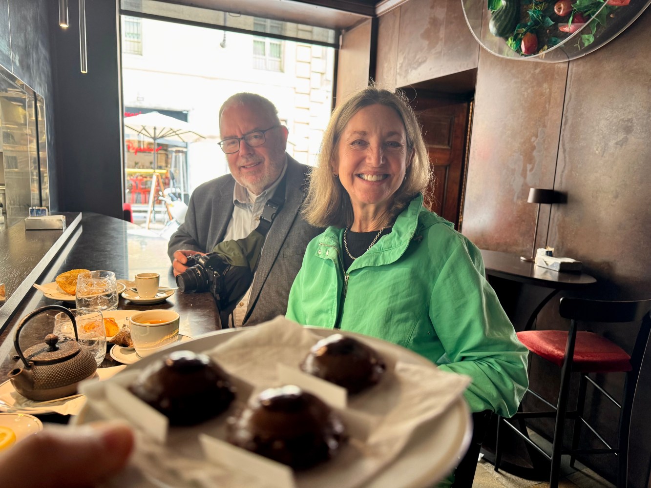 Two people smiling at a cafe with chocolate pastries in the foreground.