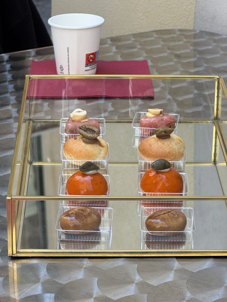 Assorted pastries in a glass display case on a table with a paper cup nearby.